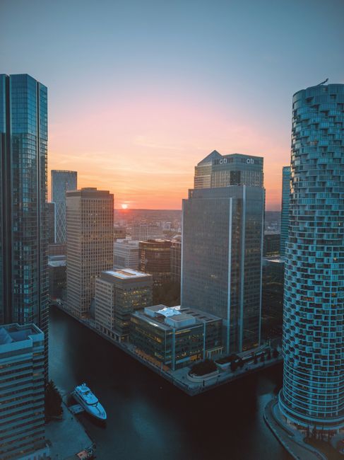A cityscape featuring a central high-rise office building with a grid-like facade and multiple illuminated windows, surrounded by other tall buildings, including HSBC and Citi bank headquarters, with 